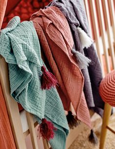 four scarves hanging on the back of a wooden bench in front of a red chair