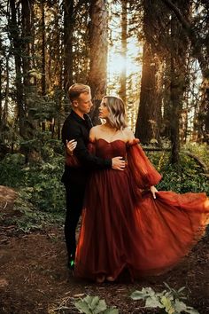 a man and woman are standing in the woods with their arms around each other as they look at each other