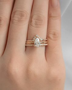 a woman's hand with two wedding rings on top of her finger and the ring has a pear shaped diamond