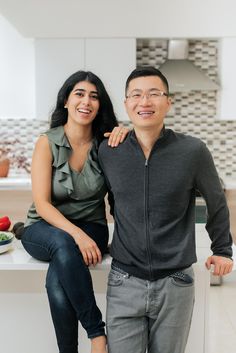 a man and woman sitting on a kitchen counter posing for the camera with their arms around each other