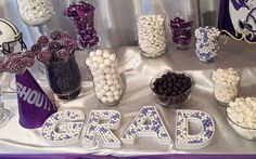 the table is set up with purple and white candy, candies, and graduation decorations