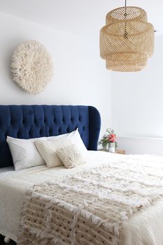 a bedroom with a blue headboard and white bedding, chandelier above the bed