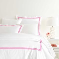 a bed with white sheets and pink trimmings in a room next to a lamp