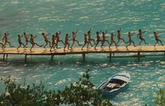 a group of people walking across a bridge over water with a boat in the background