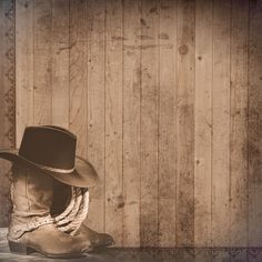 a cowboy hat sitting on top of a pair of boots in front of a wooden wall