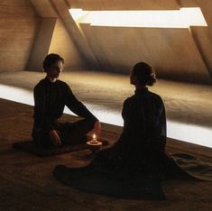 two people sitting on the floor with a lit candle in their hands and looking at each other