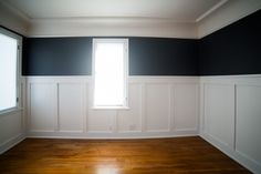 an empty room with black and white paneling on the walls, wood floors and a window