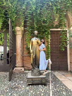 a woman standing next to a statue in front of a building with ivy growing on it