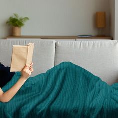 a woman laying on a couch reading a book