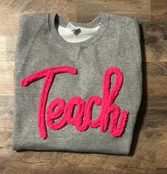 a t - shirt with the word teach written in pink thread on top of it