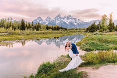 a bride and groom kissing in front of a mountain lake during their wedding photo shoot