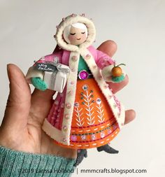 a hand holding a small doll with an orange and white coat on it's head