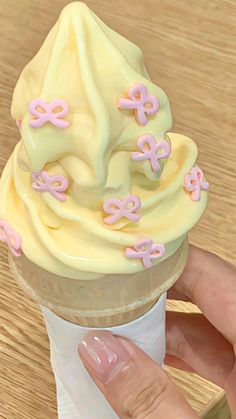 a hand holding an ice cream cone with pink and yellow decorations on it's top