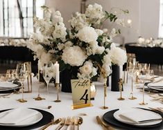 the table is set with white flowers and black plates