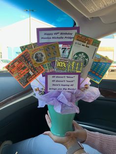 a person holding up a cup filled with lots of cards and flowers in the back seat of a car