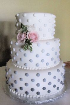 a three tiered white cake with polka dots and pink flowers on the top layer