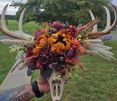 a person holding a flower arrangement in front of a deer skull with horns on it