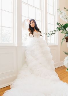 a woman in a white wedding dress standing by a window