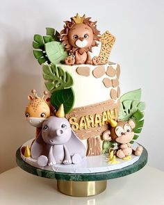 a three tiered cake decorated with animals and jungle leaves on a table next to a white wall