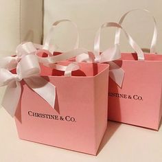 two pink bags with white bows are sitting on a table next to another bag that has the words, pristinee & co written on it