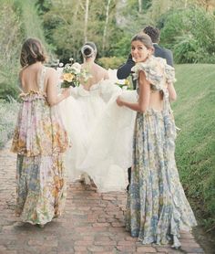 three women in dresses walking down a brick path with one holding the other's hand