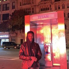 a man is standing in front of a phone booth at night with his hands on his hips