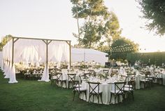 tables and chairs are set up in the grass for an outdoor wedding reception with white draping