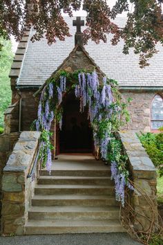 an old stone church with purple flowers growing on the front and steps leading up to it