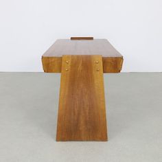 a wooden table sitting on top of a cement floor next to a white wall in an empty room