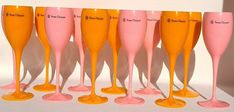 a row of pink and yellow wine glasses sitting next to each other on a white surface