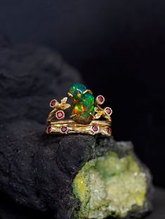 an opal and ruby ring sits on top of a rock, surrounded by stones