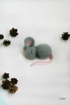 a small mouse sitting on top of a white sheet next to pine cones and needles