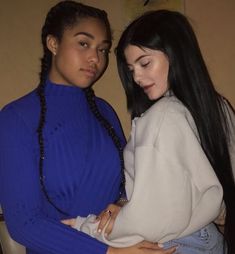 two women standing next to each other in front of a wall and one is wearing a blue sweater