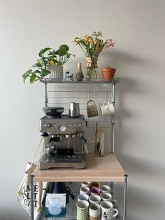 a coffee machine sitting on top of a shelf filled with pots and mugs next to a potted plant