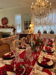 a dining room table set for christmas dinner with red and white placemats, silverware, candlesticks and napkins