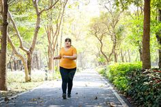 a woman walking down a path in the middle of a park with trees and bushes