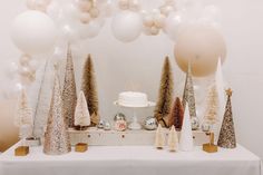 a table topped with lots of white and gold christmas trees next to balloons in the air