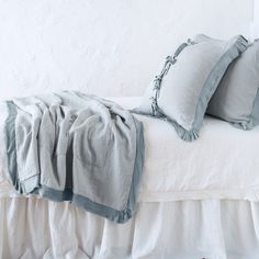 a white bed with two pillows and some blankets on it's headboard, in front of a white wall