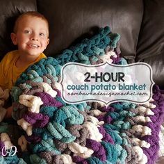 a young boy laying on top of a couch under a crocheted blanket