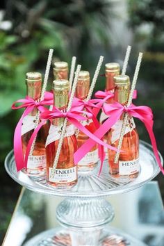 several bottles of pink wine are on a glass stand with ribbons and bows around them