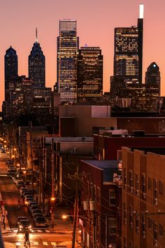 the city skyline is lit up at night, with cars parked on the side of the street