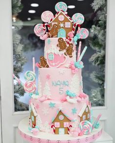 a three tiered cake decorated with pink and blue icing, gingerbread houses, lollipop canes and candies