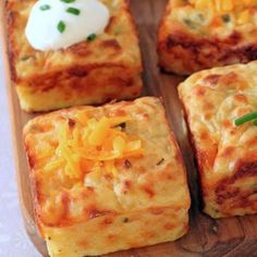 several square pieces of food on a wooden tray with cheese and sour cream toppings