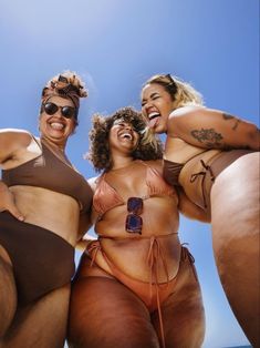 three women in bikinis posing for the camera with their arms around each other and smiling