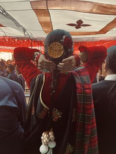 a woman dressed in red and black holding her hands over her face with other people standing around