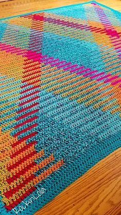 a multicolored crocheted rug is on the floor next to a wooden table