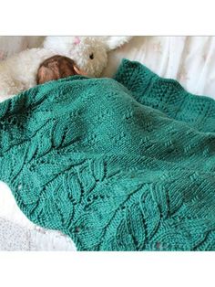 a teddy bear laying on top of a bed next to a green knitted blanket