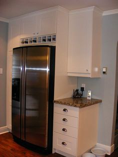 a stainless steel refrigerator in a kitchen with white cabinets and wood flooring next to a trash can