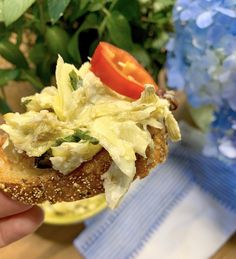 a person holding up a sandwich with vegetables on it and some sort of meat in the middle