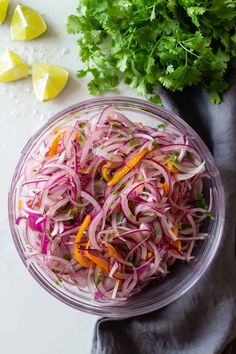 a glass bowl filled with red onions and cilantro next to lemon wedges